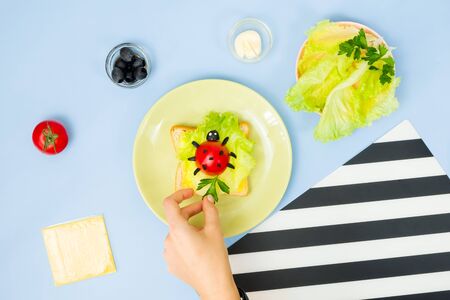 Fun food art for kids. Ladybug sandwich on blue background. How to make creative breakfast for kid at home. Step by step instruction, view from above. Step .の写真素材