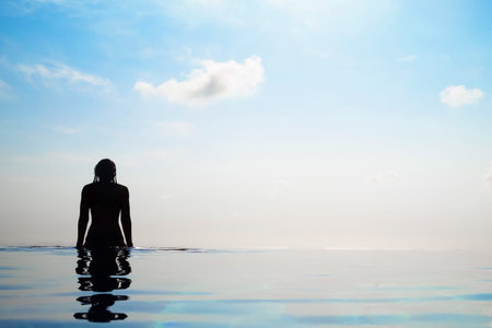 Woman relaxing in infinity swimming pool looking at view