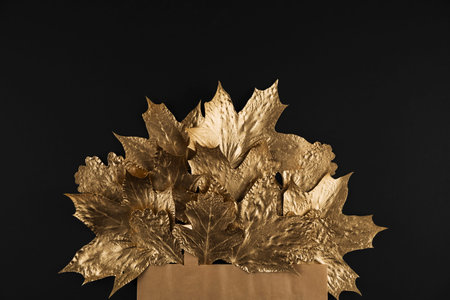 Craft package with Shiny Golden maple leaves on black background. Flat lay, top view. Minimal autumn...