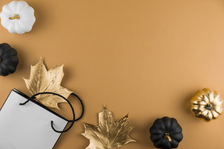 Autumn composition with golden maple leaves, decorative pumpkins and shopping bag on nude...