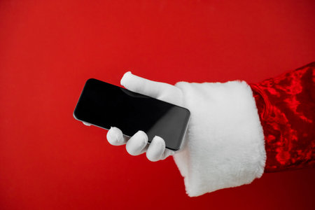 Santa Claus hand holding a smartphone with a blank screen. Mobile phone during holiday time, mockup.の写真素材