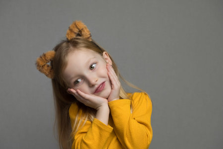 Cute blond girl with tiger ears. A headdress with tiger ears. New Year 2022. Child in a tiger costume smiles sweetly and looks at camera.の写真素材