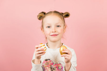 Funny little blonde girl smiling and playing with golden easter eggs on pink background. Happy...