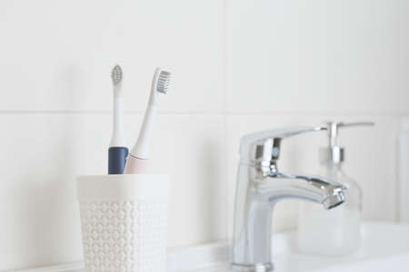 New modern ultrasonic toothbrushes in a glass on the bathroom sink. Jaw model and dental care supplies. Oral hygiene, dental and gum health, healthy teeth. Dental productsの写真素材