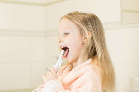 Happy smiling little girl brush teeth using ultrasonic electric toothbrush in bathroom at home. Oral hygiene, dental and gum health, healthy teeth. Daily life and routine.の写真素材