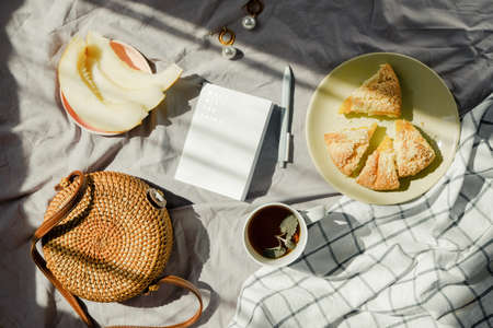 Summer picnic on a blanket with tea, fruit and pie. Wicker bag and notebook. Light green color. Summer mood inspiration.の写真素材