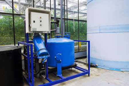 Electric motor water pump at greenhouse. Interior and equipment with pipelines and water tank in modern greenhouse. Modern greenhouse equipment for drip irrigation. Plant growth liquid tanks.の写真素材