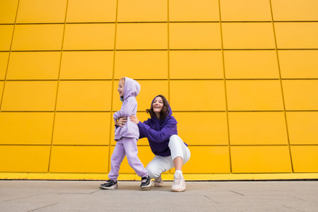 Woman in purple hoody have fun with cute girl 4-5 years old. Mommy and little daughter on yellow...