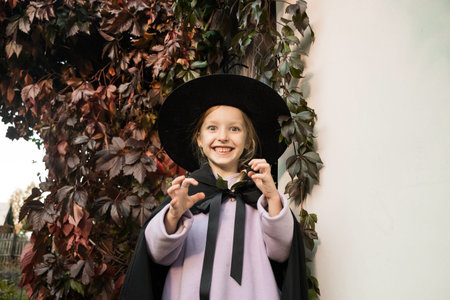 Portrait of little cute girl in witch costume and hat for halloween on fall autumn leaves...