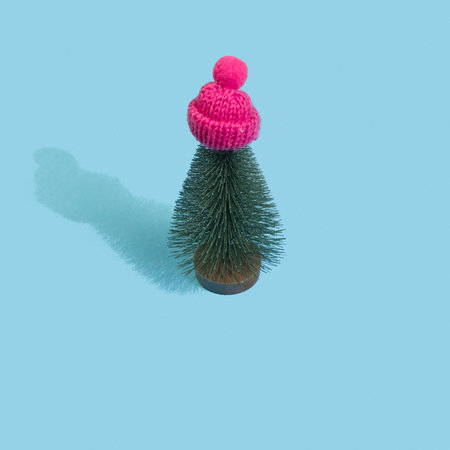 Christmas tree in pink winter cap on pastel blue background. Minimal New year concept. Magic pine...
