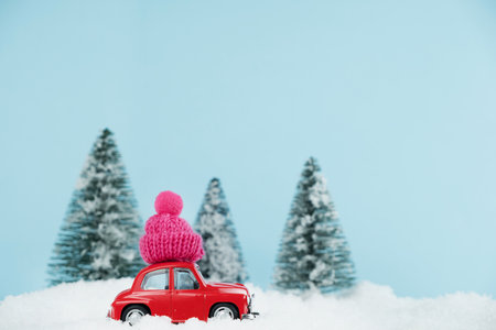 Christmas red car with knitted pink hat in a snowy pine forest. Space for text. Happy New Year card conceptの写真素材