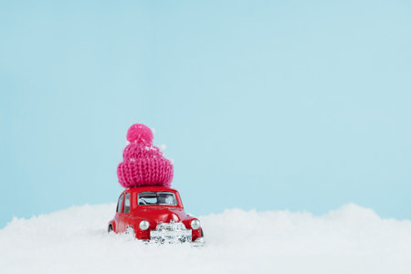 Christmas red car with knitted pink hat in a snowy landscape. Space for text. Happy New Year card conceptの写真素材