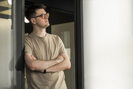 Portrait of a serious millennial male business owner in modern office. Businessman wearing glasses, looking out window. Leadership concept. Head shotの写真素材