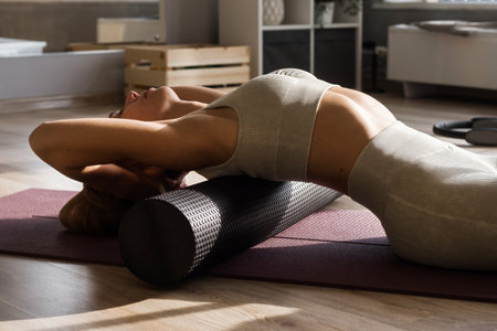 Fitness concept. Close up of woman relaxing after workout on the exercising yoga mat. Portrait of Active Woman Using Foam Roller for back and spine exerciseの写真素材