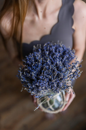 A serene woman holding a lavender bouquet in a rustic vase, embodying simplicity and natural beautyの写真素材