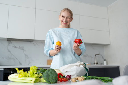 A happy woman is seen holding orange and red bell peppers in a modern kitchen settingの写真素材