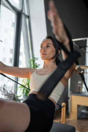 Woman doing pilates exercise on Pilates Reformer for the chest and back muscles, focusing on flexibility, strength, and control with determinationの写真素材