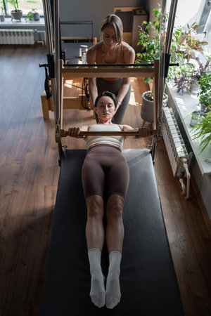 Woman doing pilates exercises with instructor on Balanced Body Cadillac machine at studio, focusing...