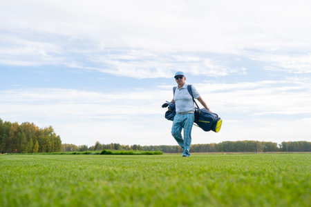 A man is leisurely walking on a beautiful golf course while carrying his golf equipment with himの写真素材