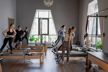 Young caucasian women exercising on pilates reformers in a bright studio. Their workout focuses on...