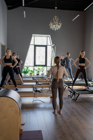 Young caucasian women exercising on pilates reformers in a bright studio. Their workout focuses on...