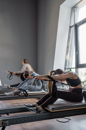 Group of caucasian women exercising with trainer on pilates reformers in a bright studio. Their workout focuses on core strength and flexibility in a modern fitness environmentの写真素材