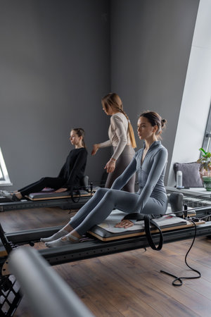 Group of caucasian women exercising with trainer on pilates reformers in a bright studio. Their workout focuses on core strength and flexibility in a modern fitness environmentの写真素材