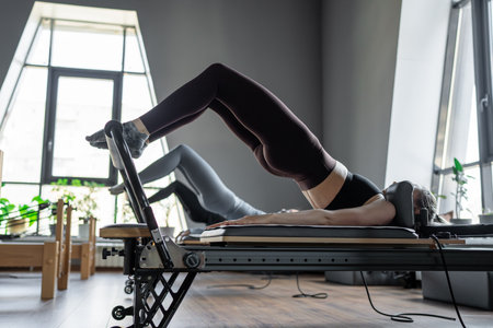 A group of woman exercises Glute bridge on a reformer bed machine in natural sunlight, focusing on pelvis and hips.の写真素材