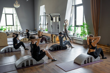 Group of women doing exercises on back spine corrector. Reformer pilates studio machine for fitness workouts in gym. Fit, healthy and strong authentical body. Fitness concept.の写真素材