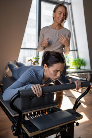Woman doing Swan exercise on Pilates Reformer for the chest and back muscles, focusing on...