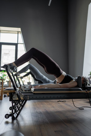 A group of woman exercises Glute bridge on a reformer bed machine in natural sunlight, focusing on pelvis and hips.の写真素材