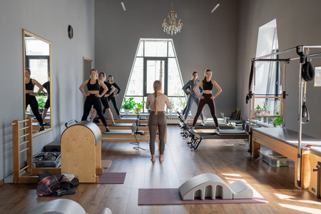 Young caucasian women exercising on pilates reformers in a bright studio. Their workout focuses on core strength and flexibility in a modern fitness environment.の写真素材