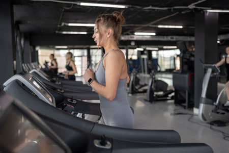 A young woman runs on a treadmill in a gym, showing her dedication to fitness and wellbeingの写真素材