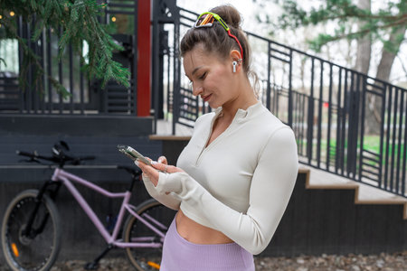 A woman in stylish activewear checks her phone, showcasing the vibrant outdoor fitness culture by...