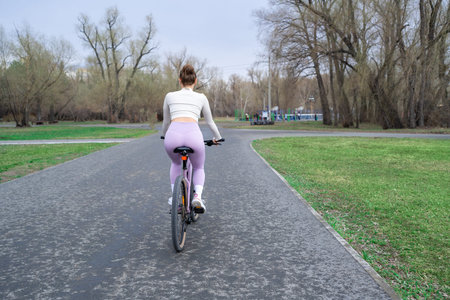 Young woman riding a bicycle in the park on the background of trees. Trendy active girl spends time...