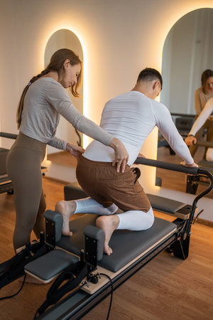 Woman Pilates Instructor Gives Guidance to a men Student While They Utilize the Reformers Equipment