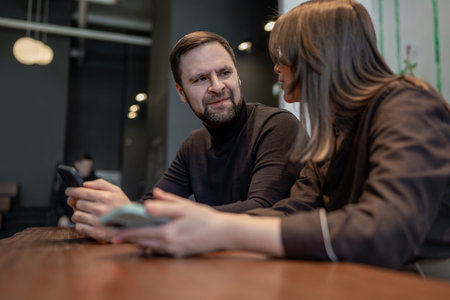 Man and woman working together on laptops at wooden benches in bright indoor space. Office teamwork,...