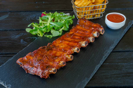 grilled pork ribs with french fries and salad on black slate plateの写真素材