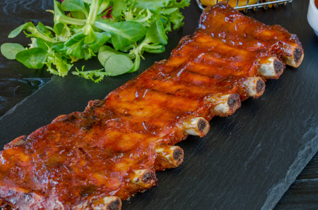 Grilled pork ribs with sauce and salad on black stone plate.の写真素材