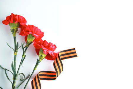 Three red carnations and St. George ribbon (Russian symbol) on a white uniform background. Greeting card for the holiday of the great victory of May 9.の写真素材