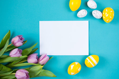 Tulips and painted Easter eggs on a blue background. Festive floral concept with clean text space....