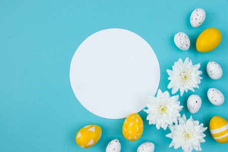 White flowers and painted Easter eggs on a blue background. Festive floral concept with clean text...
