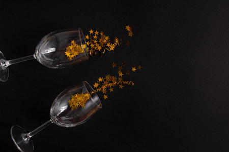 Glass goblets with golden sparkles on a black background. The concept of celebrating the new year.