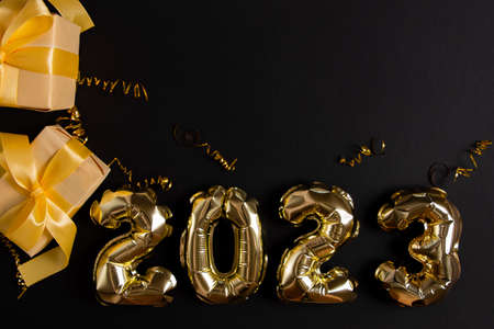Golden foil balloons in the shape of figure 2023 on a black background. The concept of celebrating the new year.の写真素材