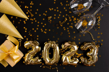 Golden foil balloons in the shape of figure 2023 on a black background. The concept of celebrating...