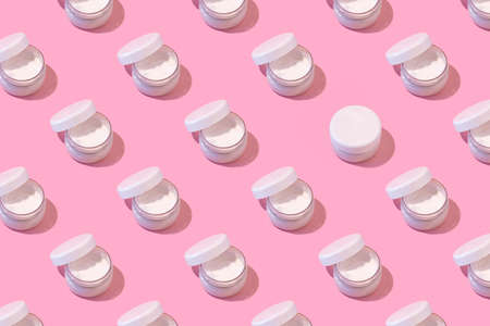 Regular pattern of open jars of cream on a pastel pink background. Minimal skincare concept.の写真素材