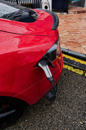Electric car on the street in red charging in the rainの写真素材