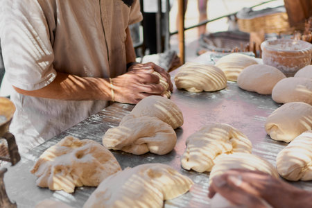 An experienced baker outdoors in the shade prepares the dough with high quality flour to make...