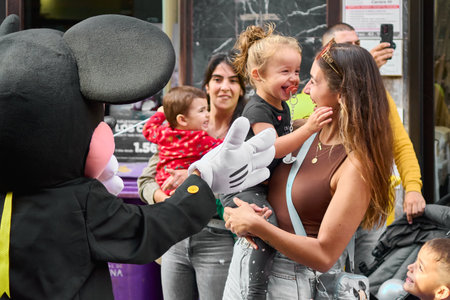 Tenerife, Spain - January 26, 2023: Middle-aged woman with a little girl in her arms smiling while an actor dressed as Mickey Mouse gestures with his handのeditorial素材