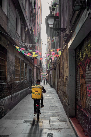 Barcelona - June 10, 2023: Glovo delivery man on a bicycle delivering through the narrow streets.のeditorial素材